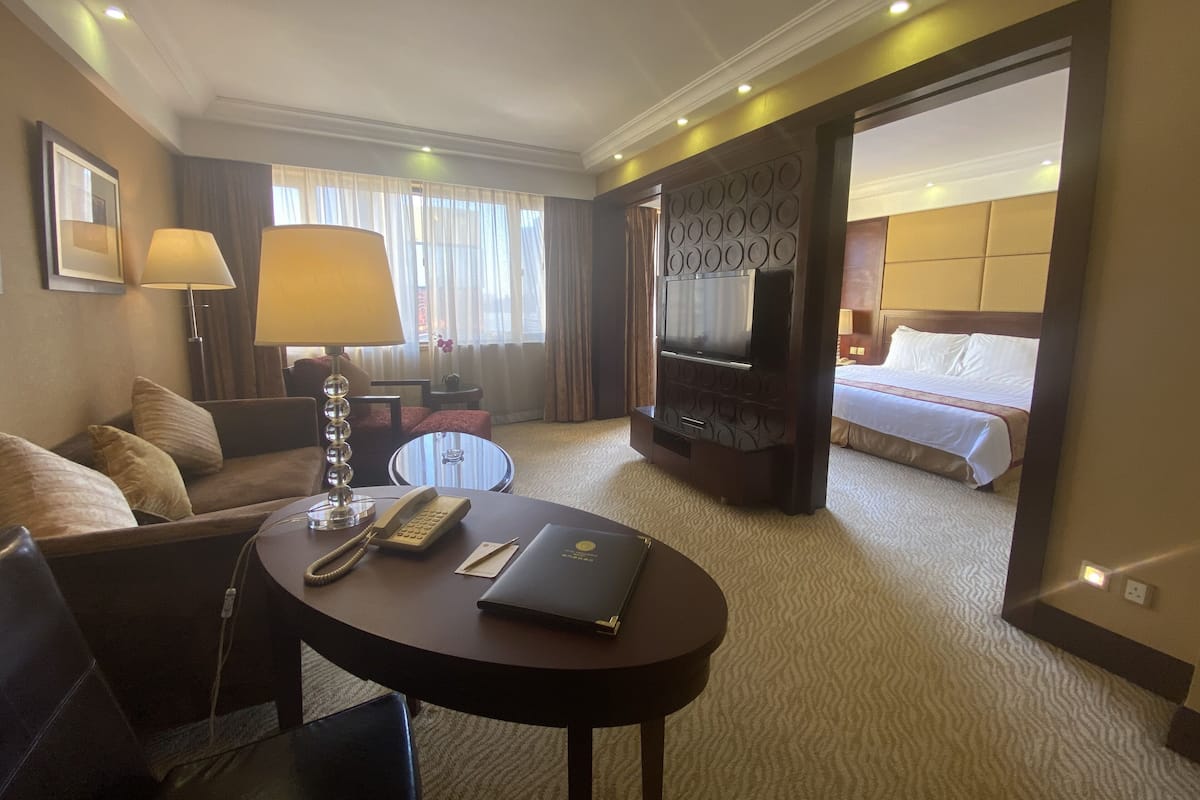 A hotel room with a bed, a TV, a desk with a lamp, a telephone, and a laptop.