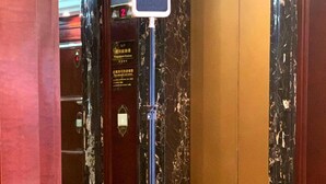 A security camera mounted on a tripod in an elevator lobby with marble walls and a marble floor. - Hotel Presidente Macau (Macau)