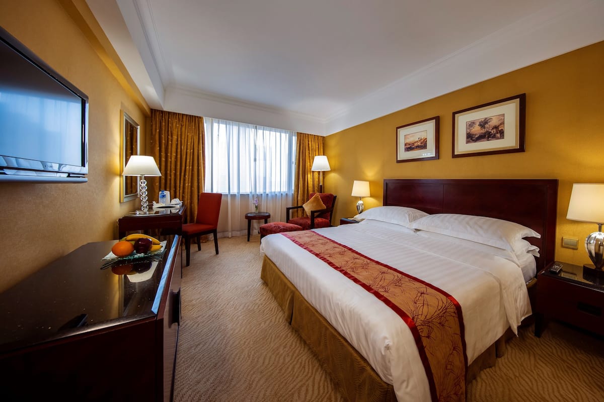 A hotel room with a large bed, a desk, a chair, a television, and two framed pictures on the wall.