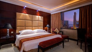 A hotel room with a large bed, a bench, a desk, and a view of the cityscape. - Hotel Presidente Macau (Macau)