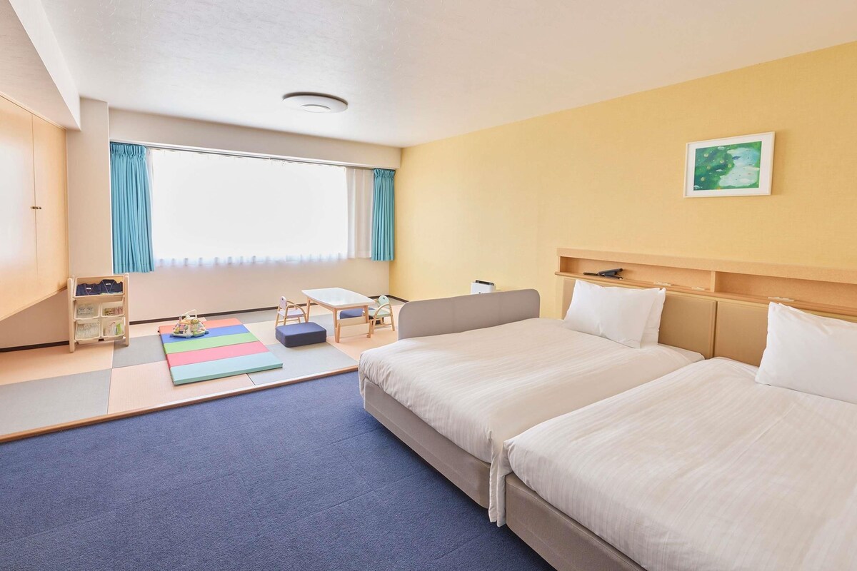 A hotel room with a bed, bedside table, and a window with curtains.