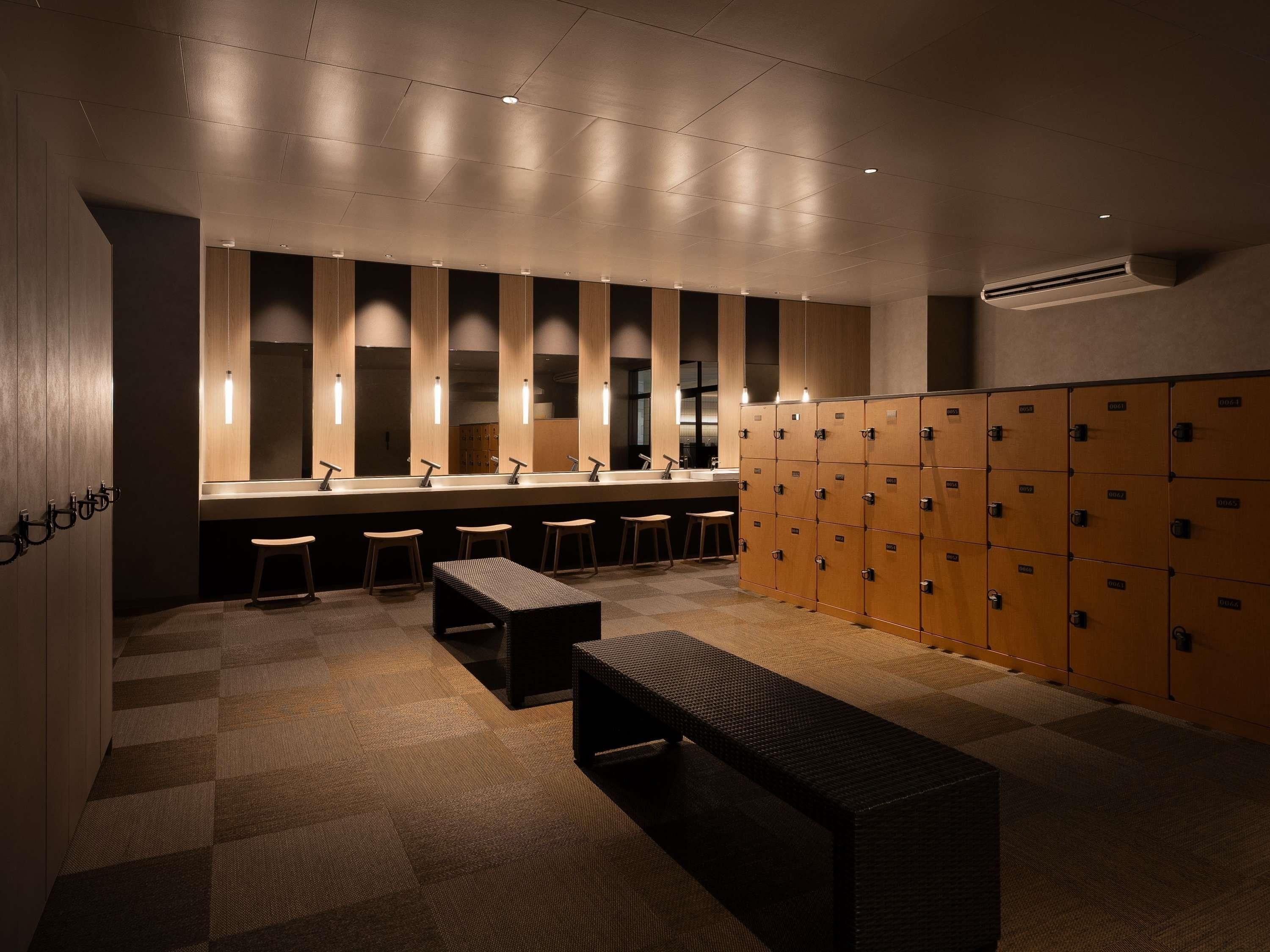 A modern restroom with wooden lockers, a bench, and a long counter with individual sinks.