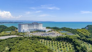 Un grande hotel con diversi piani, un parcheggio e vista sul mare e sulle montagne.