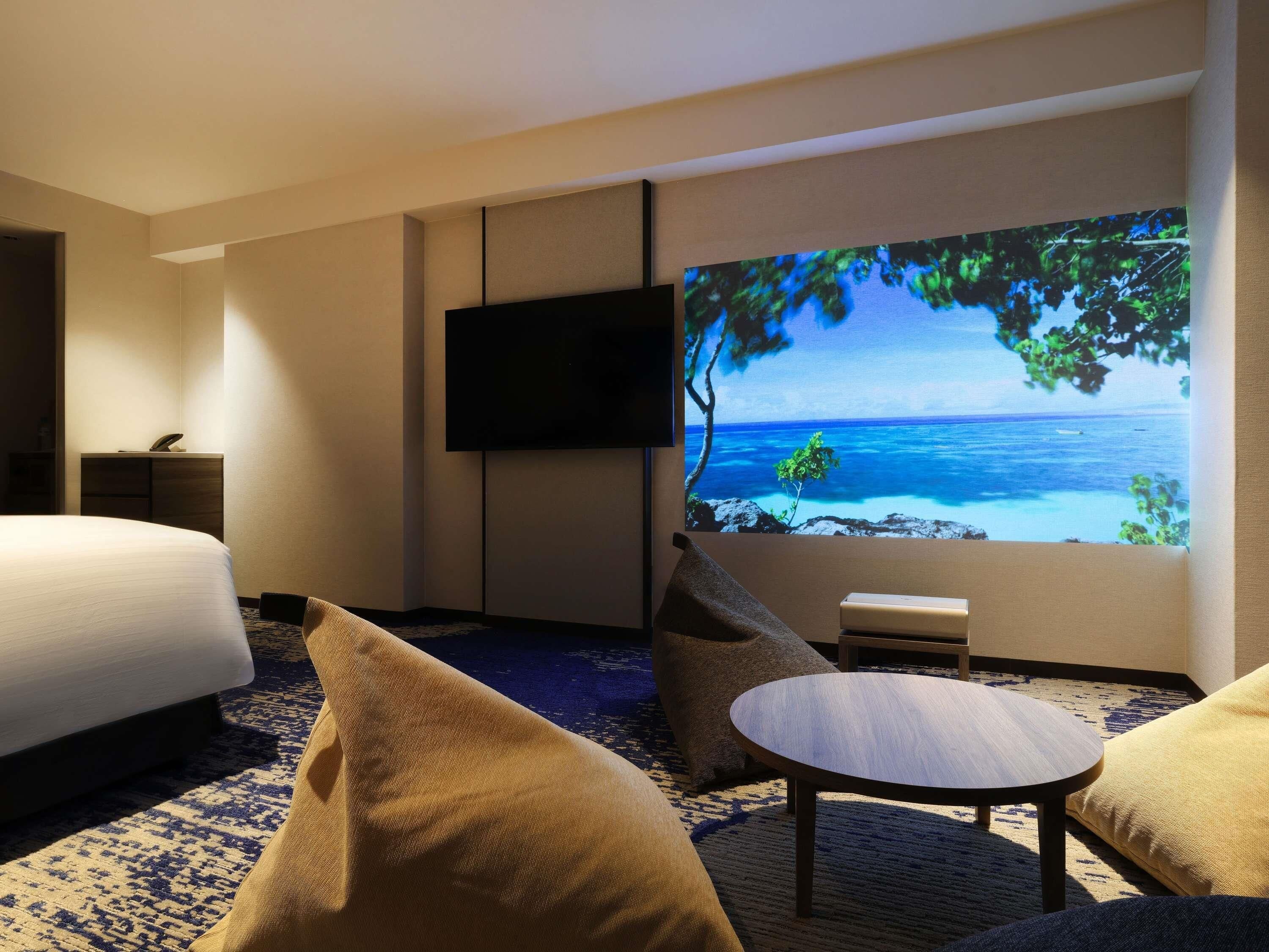 A hotel room with a bed, a flat-screen TV, a small table, and a sofa.