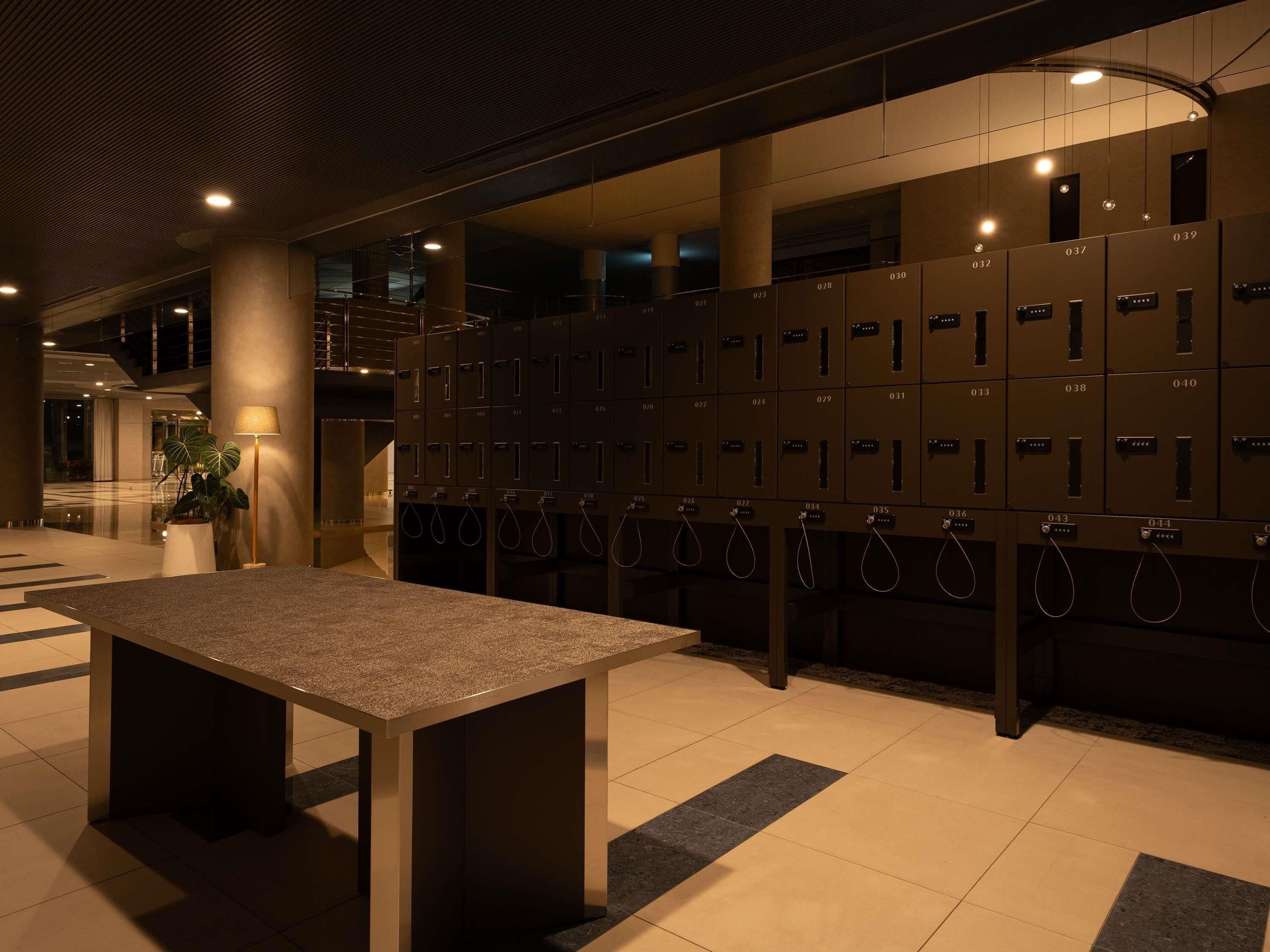 A hotel lobby with a row of lockers, a table, and a staircase in the background.