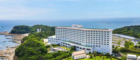 A large hotel with a pool, surrounded by lush greenery and a beach.