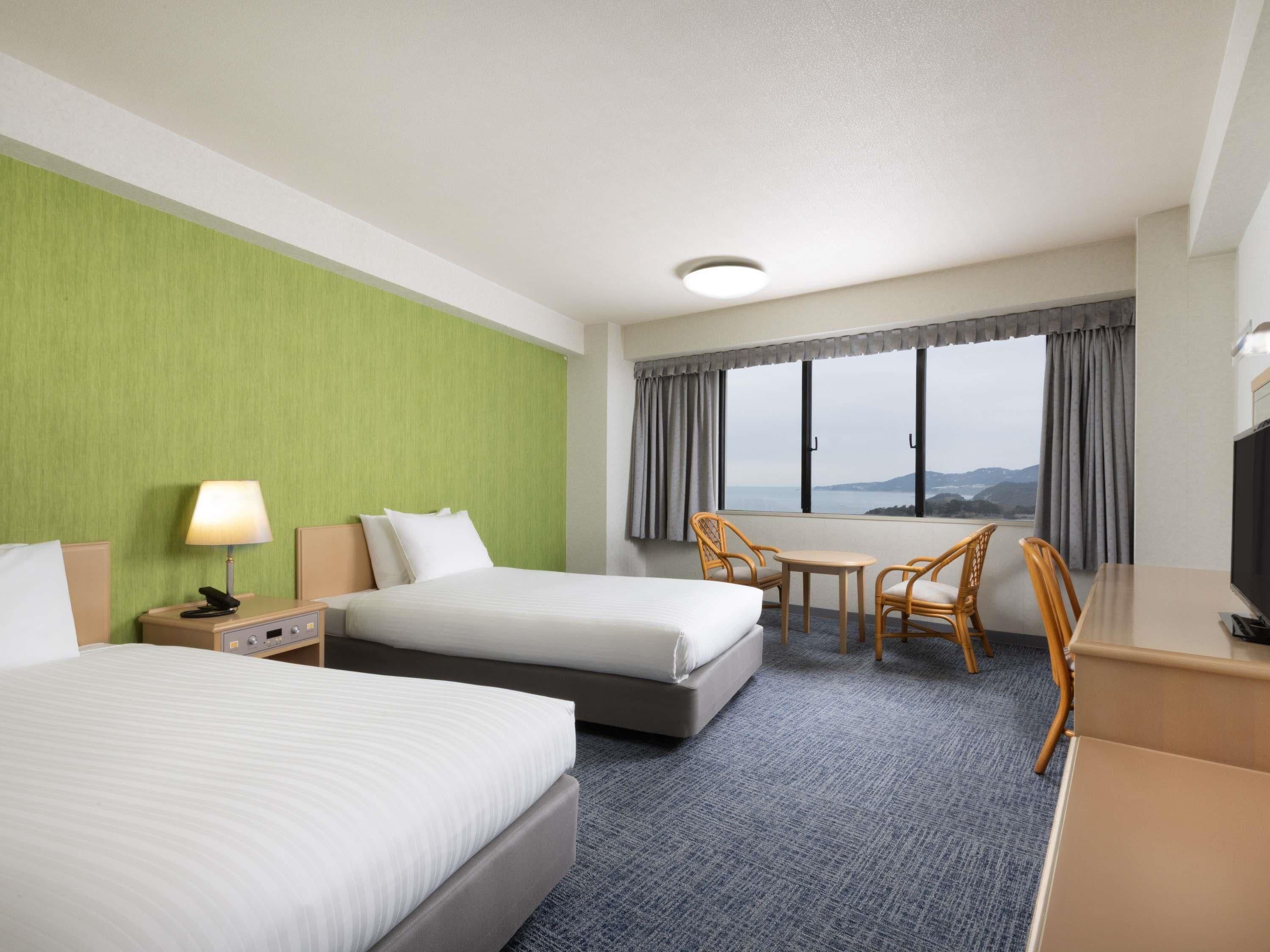 A hotel room with two beds, a desk, a television, and a view of the outdoors.