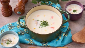 A bowl of creamy soup with vegetables and herbs, accompanied by two pepper shakers and a spoon on a wooden table.