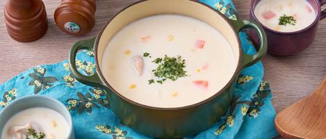 A bowl of creamy soup with vegetables and herbs, accompanied by two pepper shakers and a spoon on a wooden table.