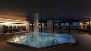 A modern indoor swimming pool with a tiled floor and a central column, surrounded by a lounge area with seating and a view of the outdoors. - Grand Mercure Wakayama Minabe Resort & Spa (Minabe)