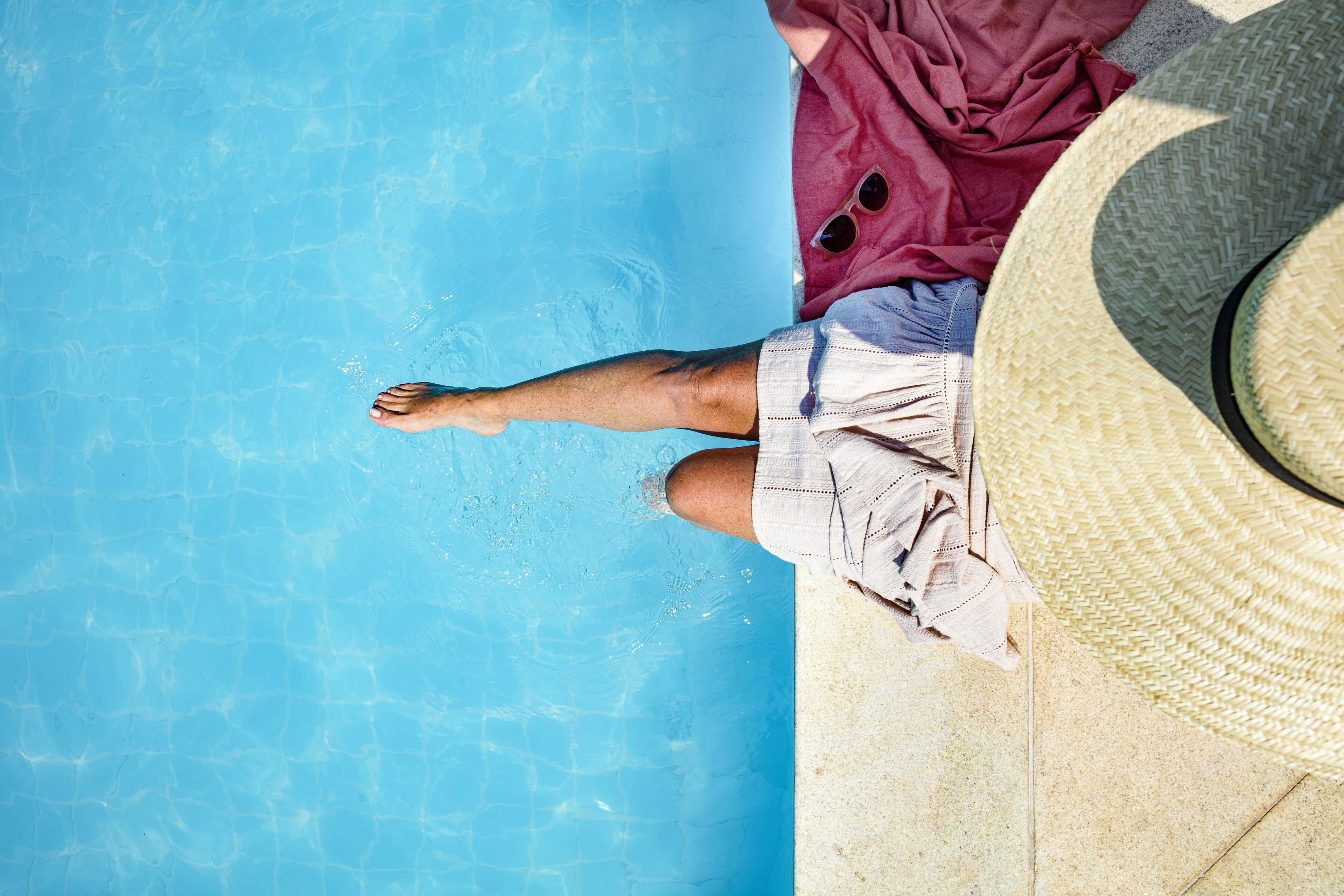 A person sitting by a pool with a hat and sunglasses, and a red cloth nearby.
