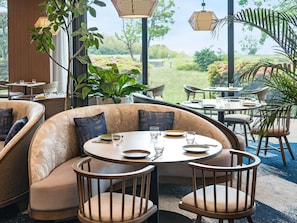 A restaurant with round tables, cushioned seating, and large windows offering a view of greenery. - Grand Mercure Wakayama Minabe Resort & Spa (Minabe)