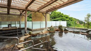Una tradizionale onsen giapponese con struttura in legno, gradini in pietra e sorgente termale cristallina.