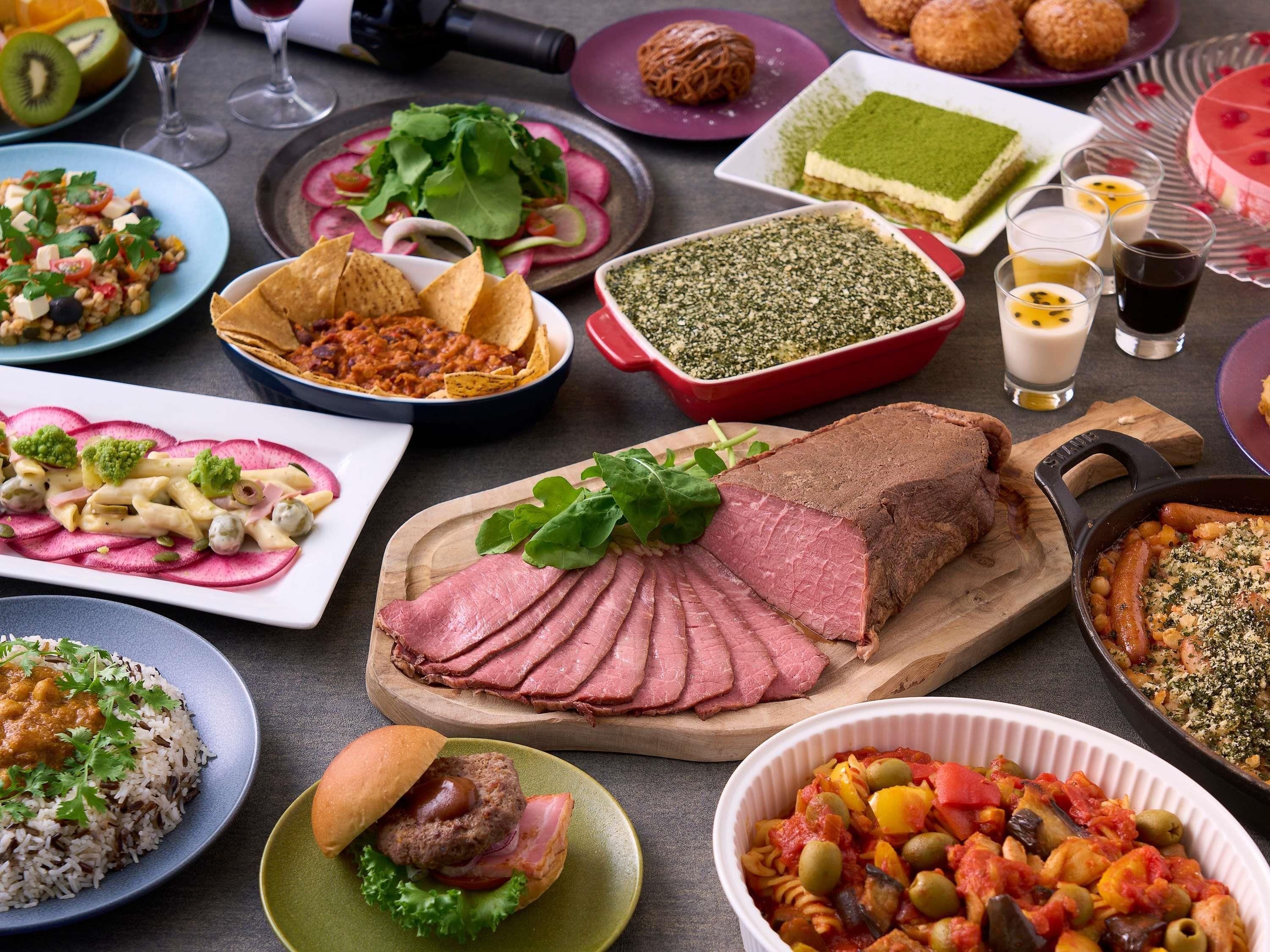 A variety of dishes and food items on a table, including a large piece of meat, pasta, and salads.