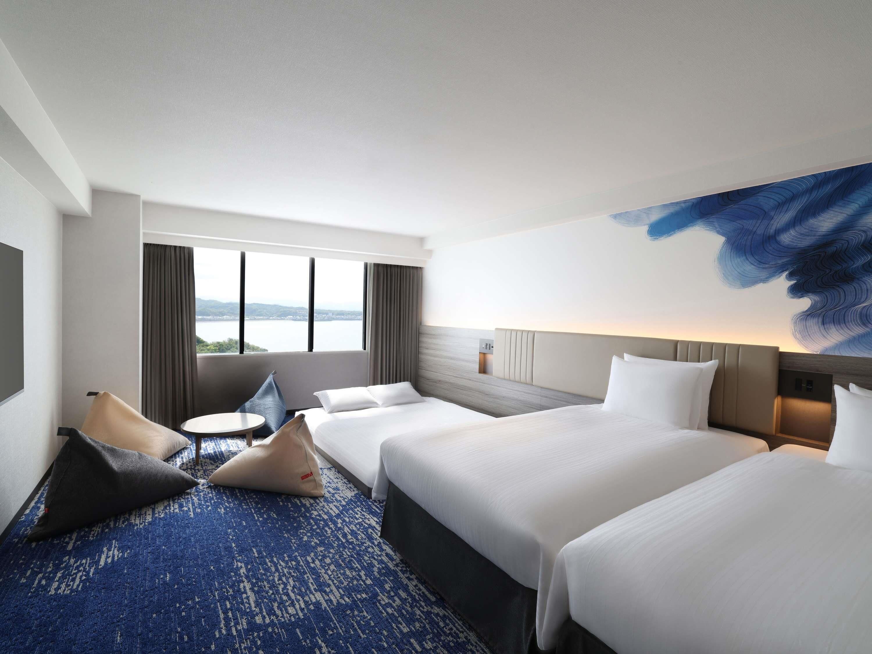 A hotel room with a large bed, a smaller bed, a desk, and a view of the outdoors.