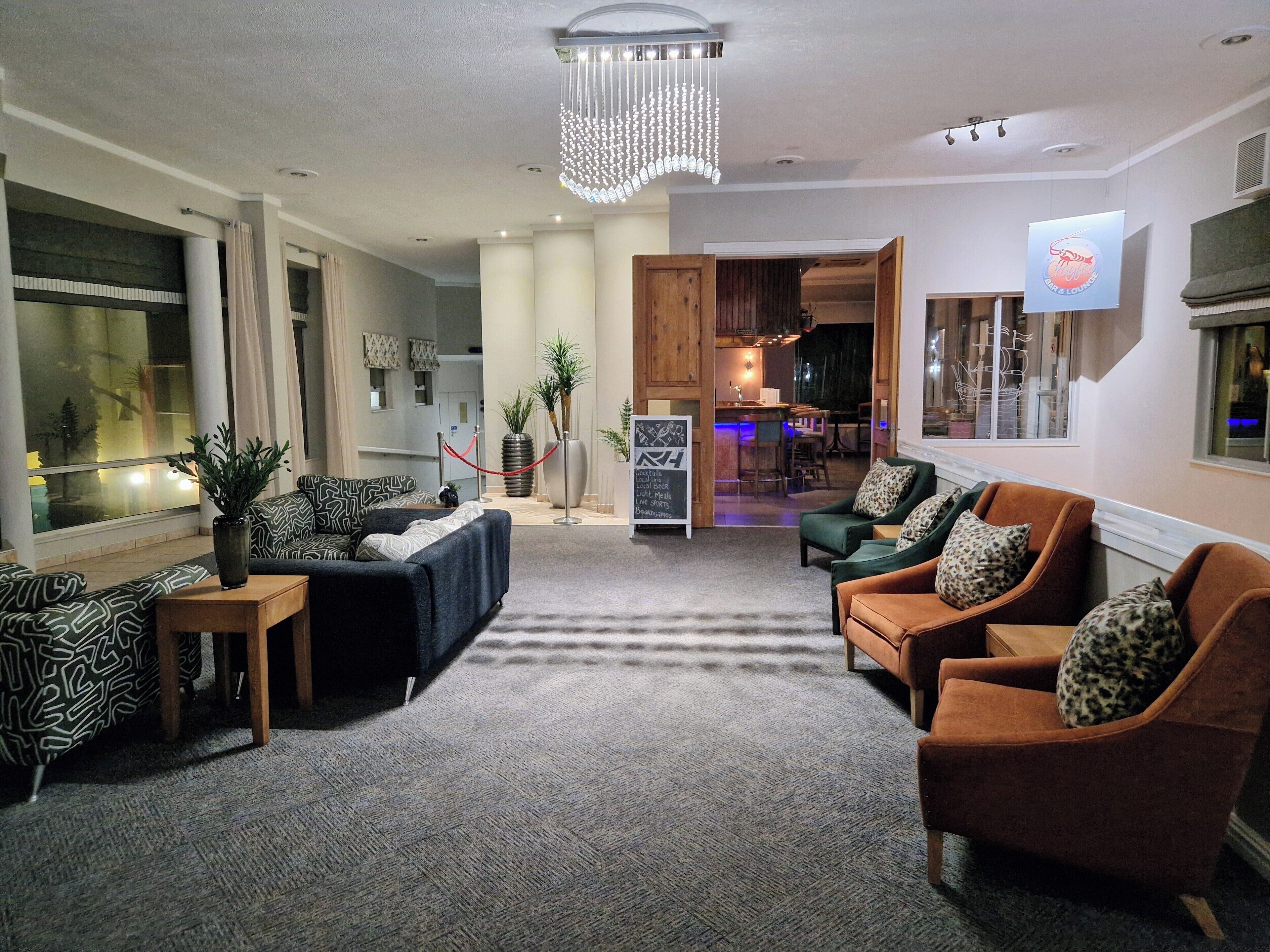 A modern living room with a sofa, armchairs, and a coffee table. There is a sign indicating the room's amenities and a view into the kitchen area.