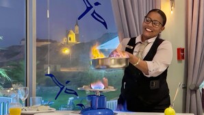 Habitación de hotel con una mesa de comedor dispuesta para dos personas, un adorno azul y vistas a una iglesia y colinas a través de la ventana.