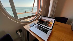 Un ordenador portátil sobre una mesa de madera, con vista al mar a través de una ventana.