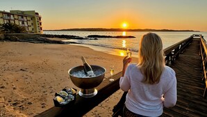 Escena de playa con atardecer, un muelle y una persona sosteniendo una copa de champán.