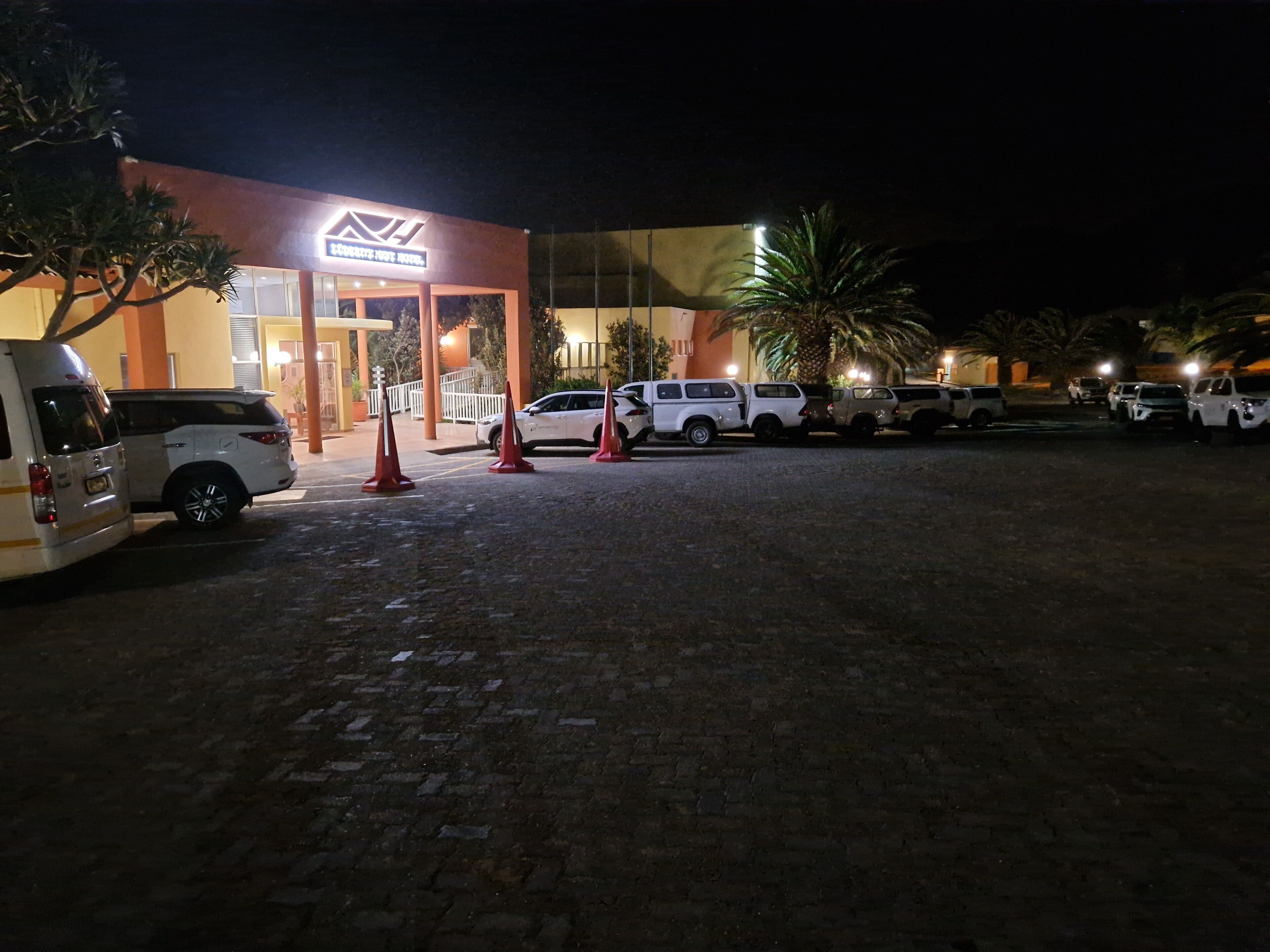 L'ingresso di un hotel dal design moderno, con facciata in vetro e un'area parcheggio con diversi SUV.