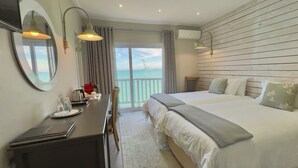 Habitación de hotel con una cama grande, un escritorio con una computadora portátil, una silla y vista al mar a través de una puerta corrediza.