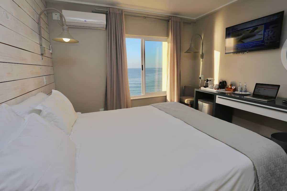 A hotel room with a bed, a desk with a laptop, a TV, and a view of the sea.