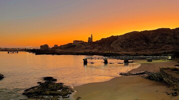 Atardecer costero con un puente, costa rocosa y un edificio con torre.