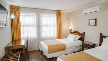 Habitación de hotel con dos camas, un escritorio de madera, una silla y un ventanal con cortinas.
