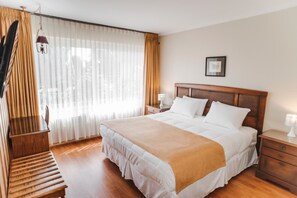 A hotel room with a large bed, wooden floor, a nightstand, a lamp, and a picture on the wall. - Hotel Melillanca (Valdivia)