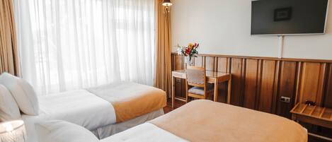 Habitación de hotel con dos camas, un escritorio, una silla, un televisor y una ventana con cortinas.