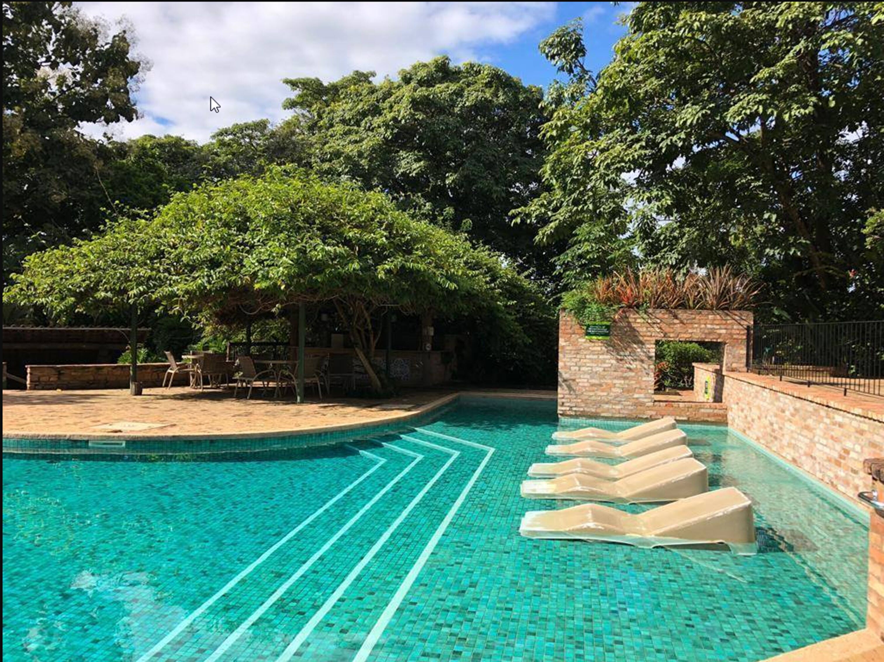 Piscina com água azul cristalina, rodeada por árvores e um muro de tijolos.