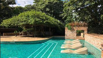 Piscina com água azul cristalina, rodeada por árvores e um muro de tijolos.