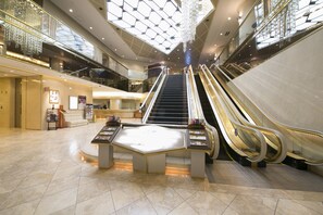 Een ruime atrium met meerdere roltrappen, een centraal presentatiegebied en een hoog plafond met dakramen.