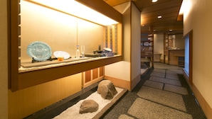 Een hotelgang met een receptiebalie, een kleine binnentuin met rotsen en zand, en een houten receptiebalie met een glazen vitrine.