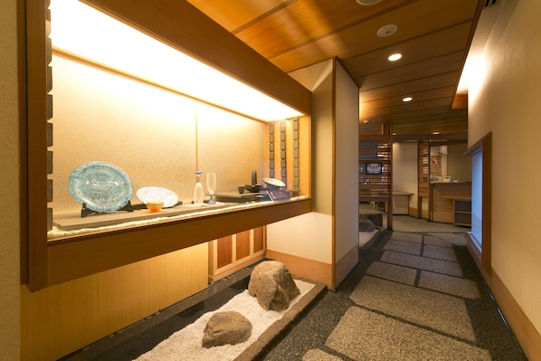A hotel corridor with a reception desk, a small indoor garden with rocks and sand, and a wooden reception desk with a glass display case.