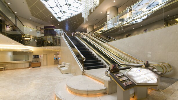 Een ruime lobby met een centrale trap, een receptiebalie en een glazen vitrine.