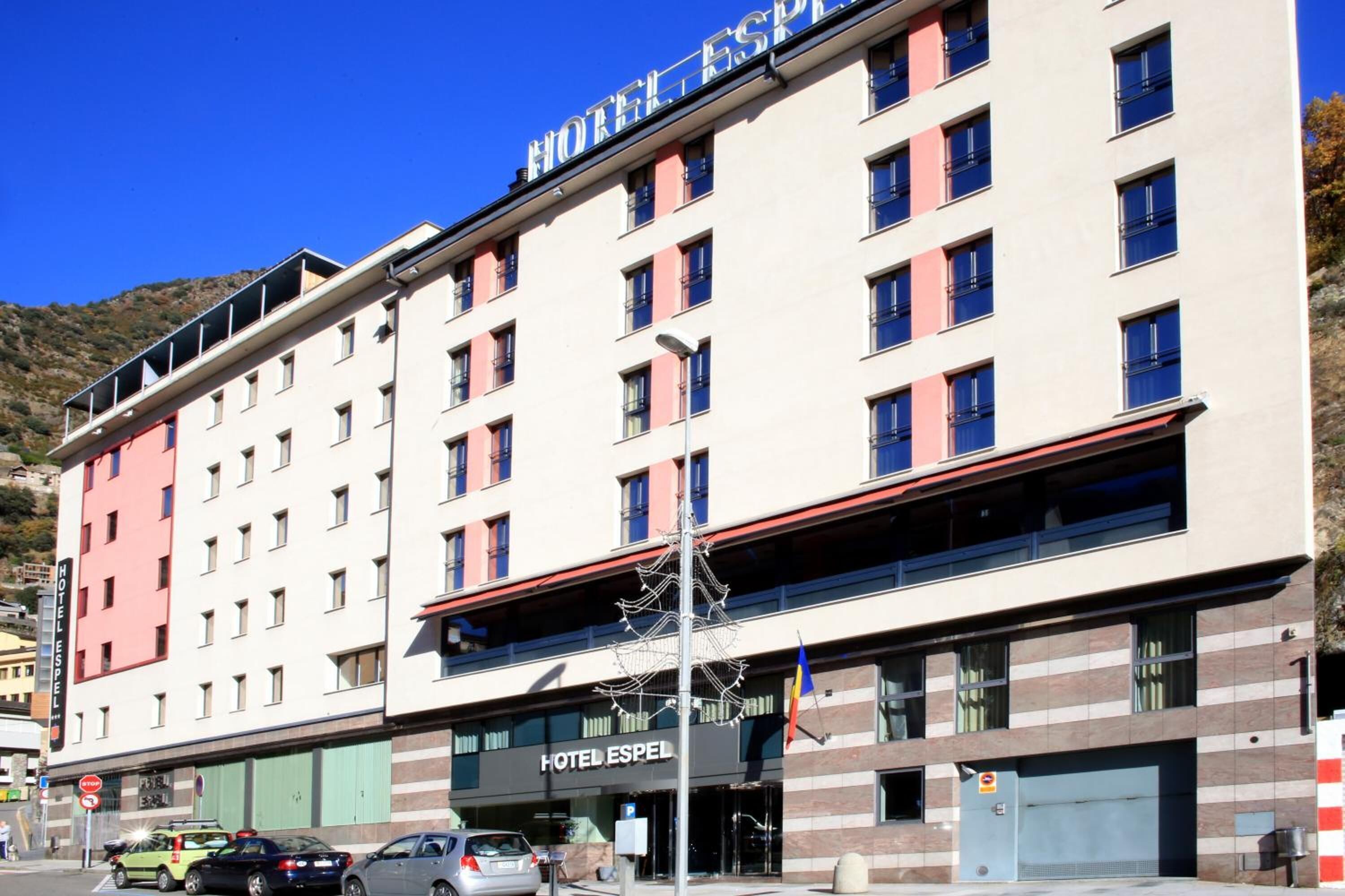 Un hotel de varios pisos con un llamativo letrero que dice "HOTEL ESPER", que presenta una fachada moderna con grandes ventanales y un techo plano.