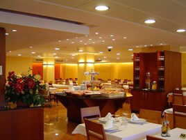 Une salle à manger d’hôtel avec de nombreuses tables préparées pour le petit-déjeuner, un buffet et un grand arrangement floral.