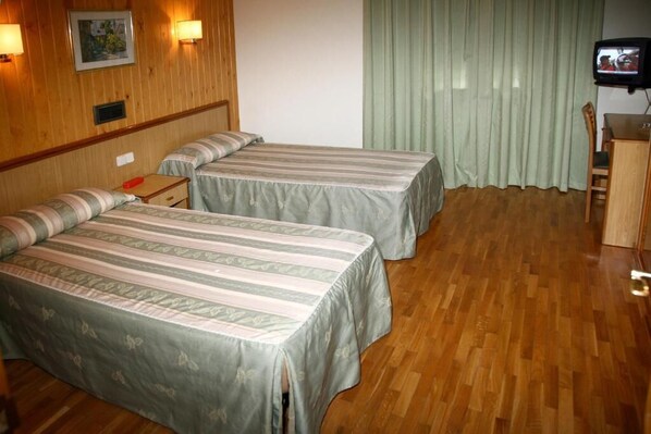 Habitación de hotel con dos camas, piso de madera, escritorio, una silla, televisor y ventana con cortinas.