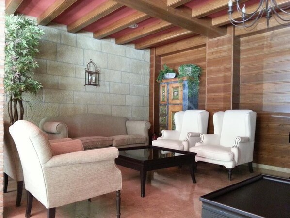 A cozy living room with a stone wall, wooden ceiling beams, a glass coffee table, and white leather sofas. - Villa de Canfranc (Canfranc)