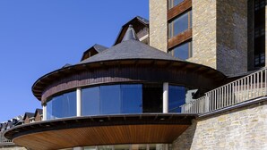 A modern building with a prominent tower, large windows, and a curved wooden structure. - Snö Aragon Hills (Sallent de Gallego)