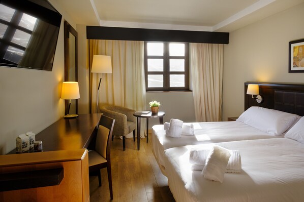 Une chambre d’hôtel avec deux lits, un bureau, une chaise, une télévision et une fenêtre avec des rideaux.