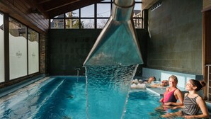 An indoor swimming pool with clear water, a wooden ceiling, and large windows. - Snö Aragon Hills (Sallent de Gallego)
