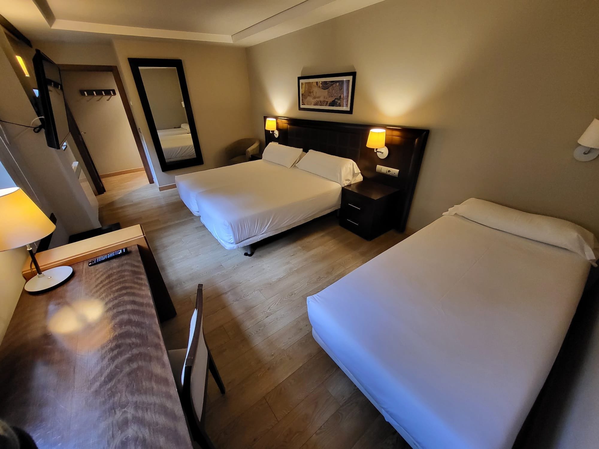 A hotel room with two beds, a desk, a chair, and a mirror.