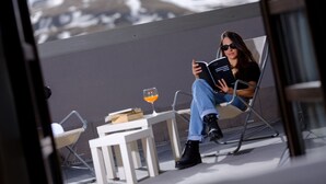 A person sitting on a chair reading a book, with a glass of orange juice and a book on a small table beside them. - Snö Aragon Hills (Sallent de Gallego)