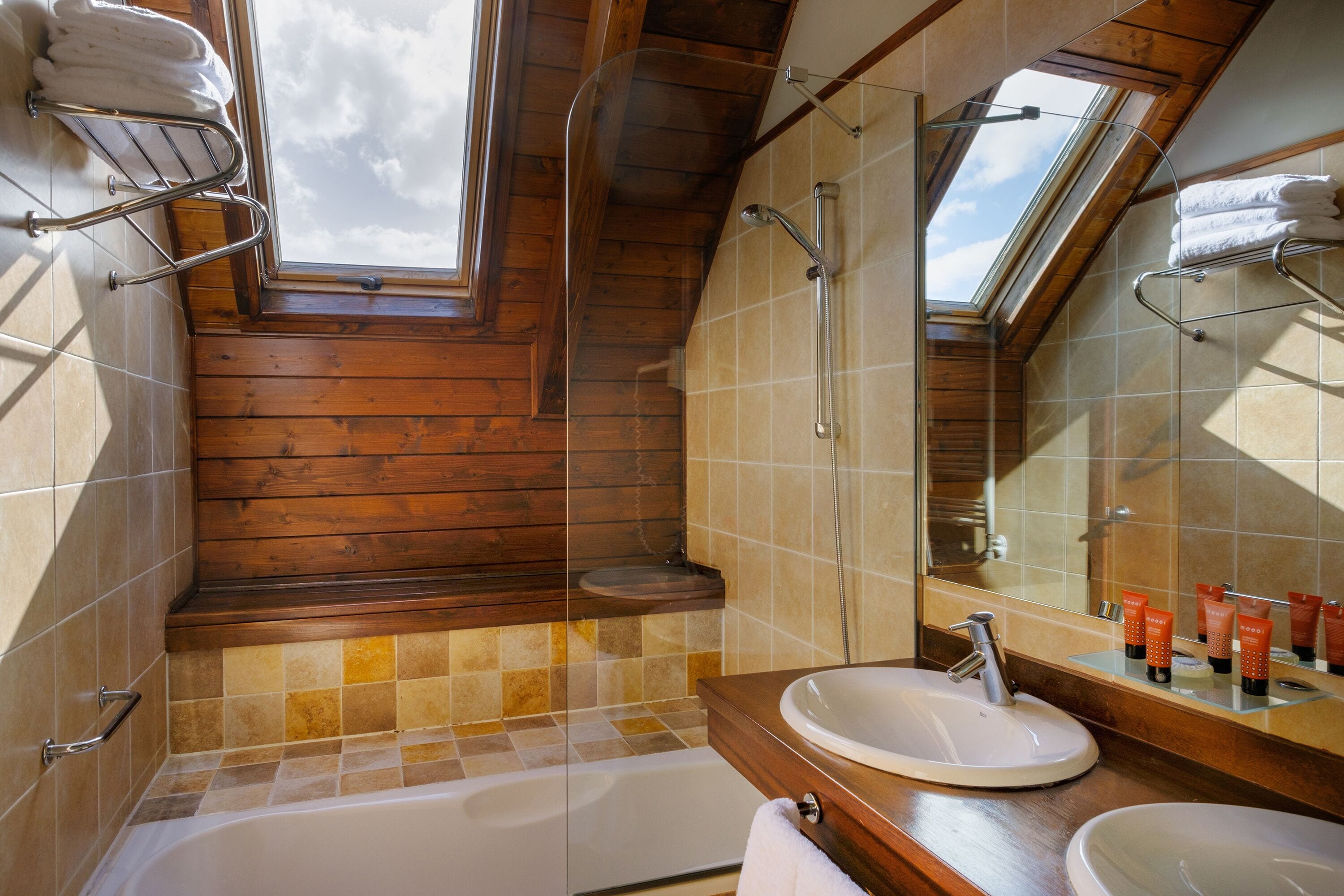 Een moderne badkamer met dakraam, bad, wastafelmeubel en grote spiegel.