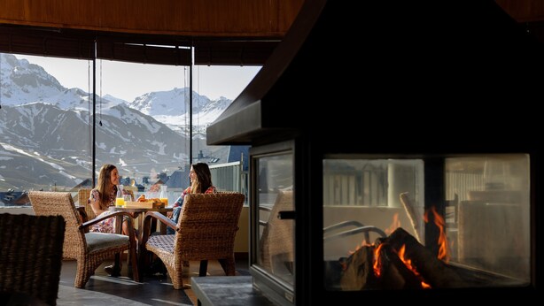 A cozy room with wicker furniture, a fireplace, and a large window overlooking snow-capped mountains. - Snö Aragon Hills (Sallent de Gallego)