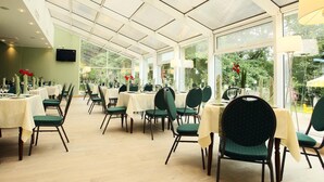Ein Restaurant mit Tischen, Stühlen, großen Fenstern und einer Decke mit Oberlichtern.