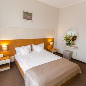 Ein Hotelzimmer mit Bett, Nachttischlampen, einem Nachttisch, einem Spiegel und einer kleinen Pflanze auf einem Regal.