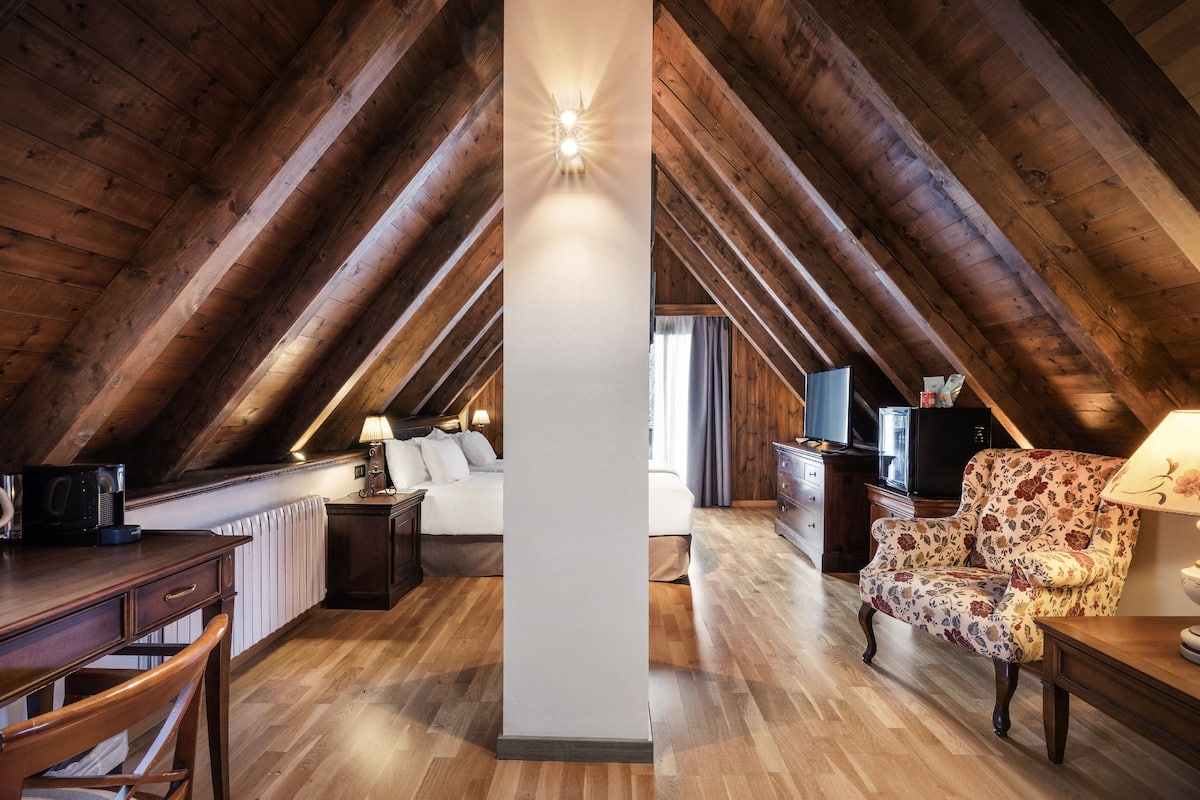 Un dormitorio acogedor en el ático con vigas de madera, una cama, un escritorio y una silla.